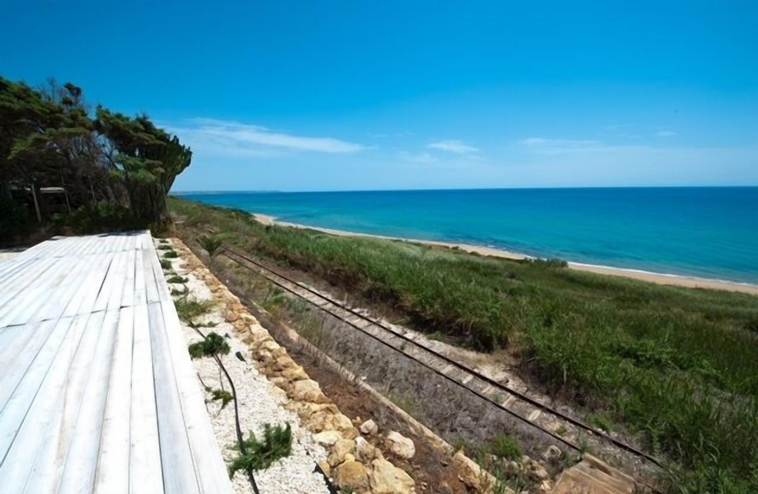 Eine Holzterrasse mit Blick auf einen Strand, bewölkter Himmel.