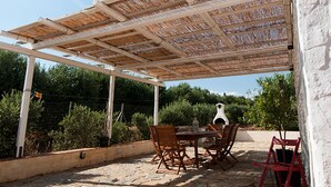 An outdoor patio with a pergola, stone flooring, wooden and red chairs, and a table with a lantern.