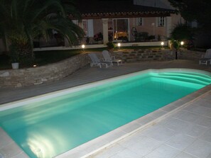 Une piscine rectangulaire bordée d’un muret en pierre et dotée d’un espace patio avec des chaises et des plantes en pot.