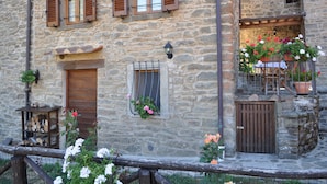 Un bâtiment en pierre avec des volets en bois, un petit balcon agrémenté de plantes en pot et une porte en bois.