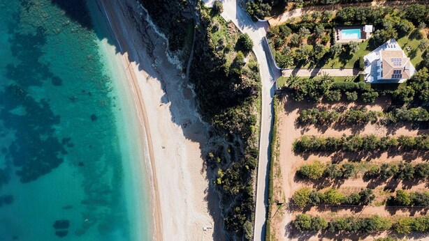 An aerial view of a coastal property with a beach, a road, and a large building with a pool. - Panoramic villa with pool in front of the beach (Scopello)