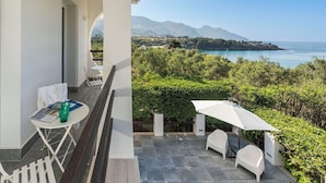 A balcony with a table and chairs, a white umbrella, and a view of the sea and mountains. - Panoramic villa with pool in front of the beach (Scopello)
