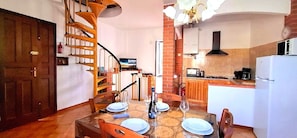 A dining area with a spiral staircase, a kitchen with a brick wall, and a white refrigerator. - Old stone house with sea view (pompeiana)