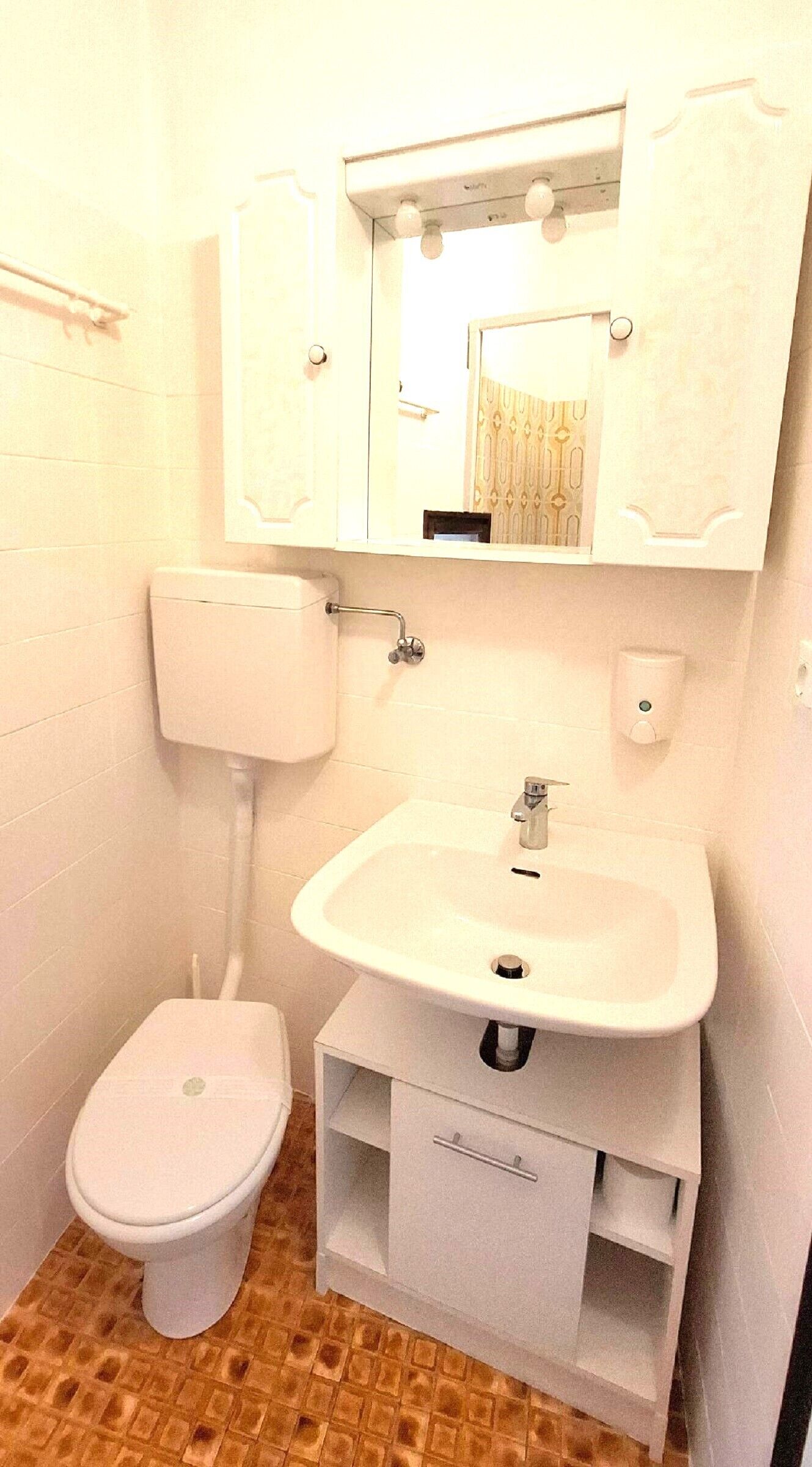 Un baño con inodoro, lavamanos, espejo y armario.