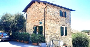 A stone building with a sloped roof, a small porch with potted plants, and a parked car. - Old stone house with sea view (pompeiana)