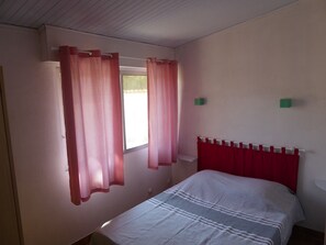 Een slaapkamer met een bed, rode gordijnen, een raam en een wit hoofdeinde.