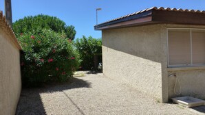 A residential area with a house featuring a gravel driveway, a small concrete step leading to a door, and a window with blinds.