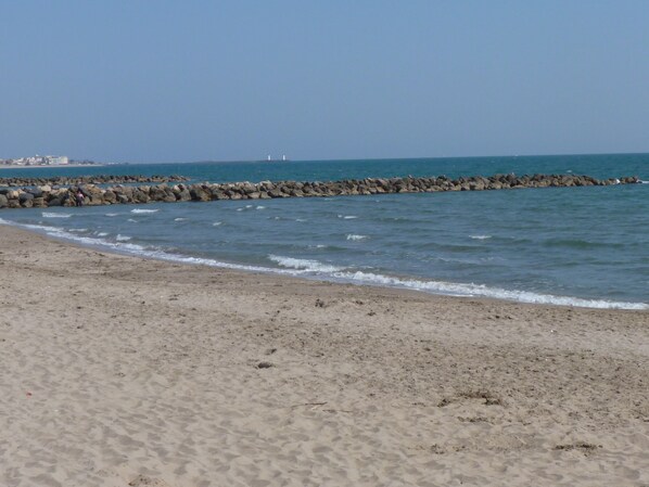 Een zandstrand met kalme golven, een rotsenrij en een heldere lucht.