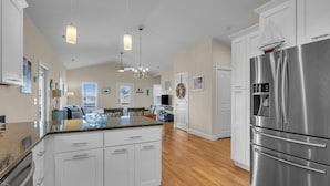 A spacious kitchen with a large stainless steel refrigerator, white cabinetry, and a wooden floor. - Bonne Mer: Three bedroom, two bathroom house in Oak Island close to shopping and (Oak Island)