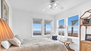 Un dormitorio con cama, una silla, una mesita, un mueble para televisión y ventanas amplias con vistas.
