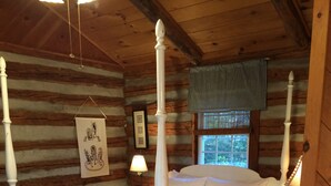 A log cabin bedroom with a four-poster bed, wooden floors, and a checkered bed skirt.