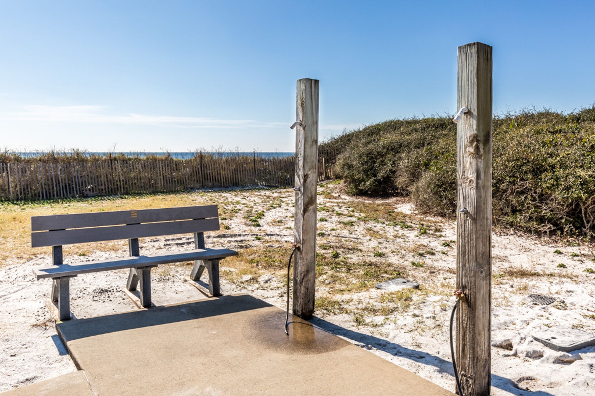 A bench and wooden posts in a sandy area with a clear sky.