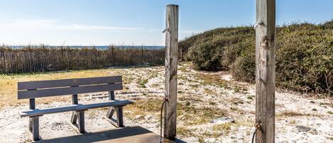 A bench and wooden posts in a sandy area with a clear sky.