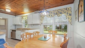 Une cuisine avec des meubles blancs, une table à manger en bois avec des chaises et un luminaire suspendu.