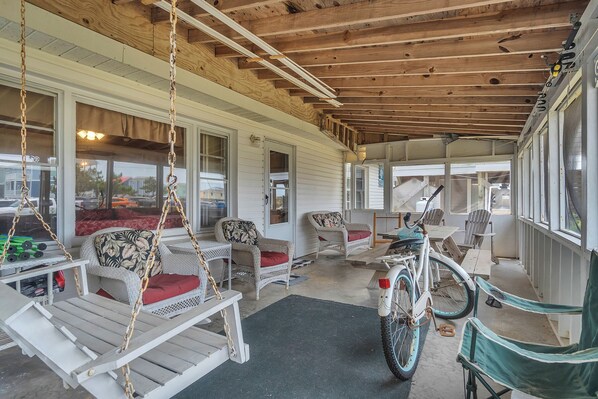 A covered porch with wicker furniture, a bicycle, and a view of the street. - Papa's Place: A Stone's Throw to the Beach! (Oak Island)