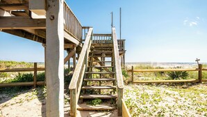Una escalera de madera que conduce a una zona de playa con un cerco de madera y un sendero arenoso.