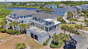 A large, multi-story house with a prominent balcony, a garage, and a view of a body of water. - Turtle Soup: Oceanfront home in East Beach with plenty of ocean leading windows (Oak Island)