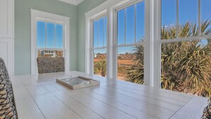 A room with large windows, a wooden table, and a patterned bench. - Turtle Soup: Oceanfront home in East Beach with plenty of ocean leading windows (Oak Island)