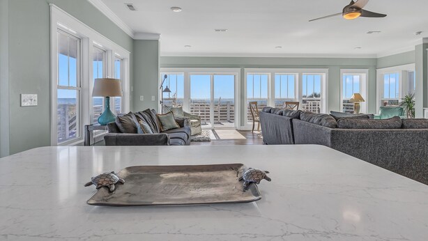 A spacious living area with a large island, a ceiling fan, and a view of the outdoors. - Turtle Soup: Oceanfront home in East Beach with plenty of ocean leading windows (Oak Island)