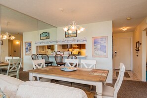 A dining area with a wooden table and white chairs, a kitchen in the background, and nautical-themed decorations.