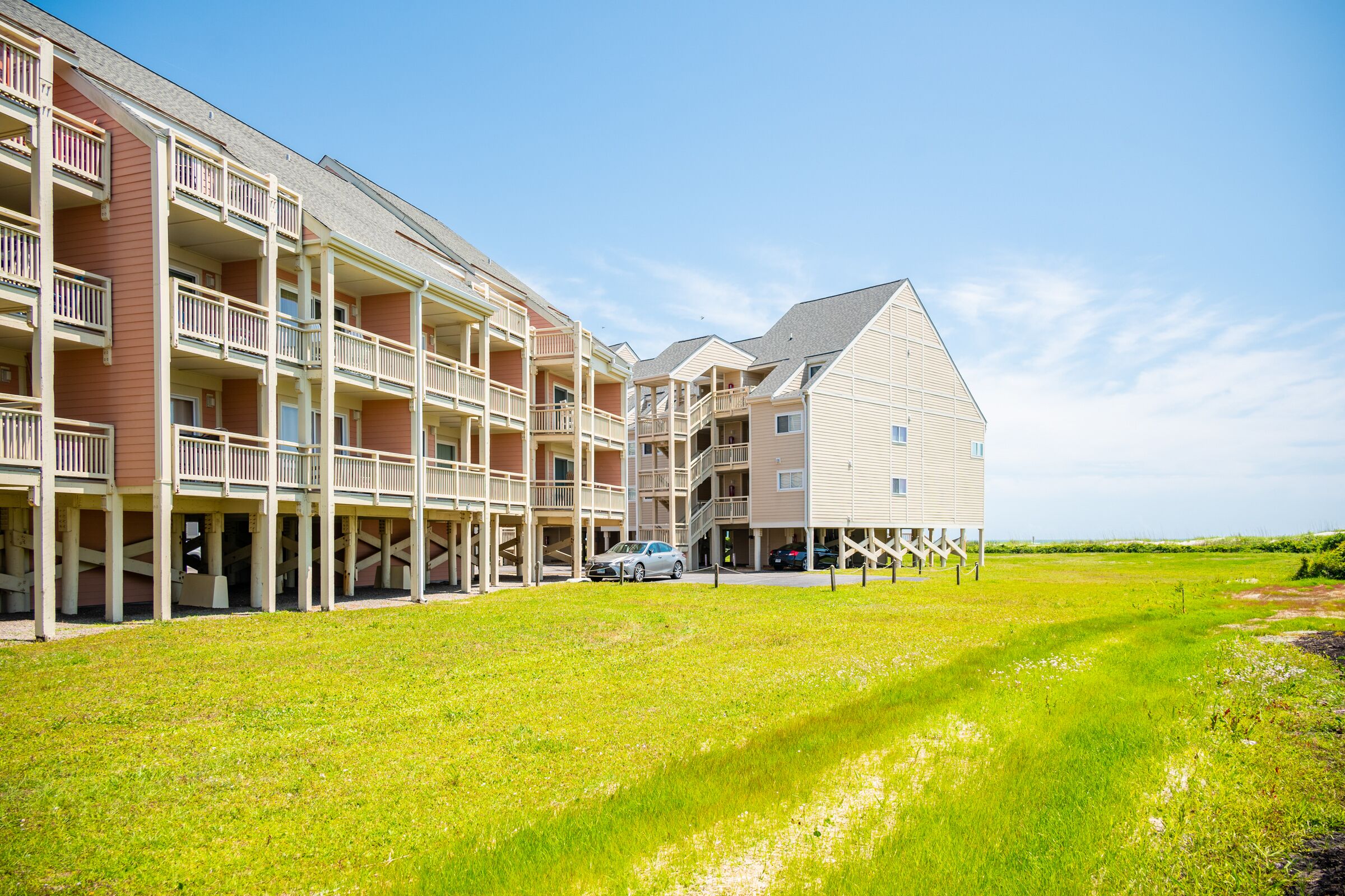 A multi-story hotel with balconies, a grassy courtyard, and a parking area.