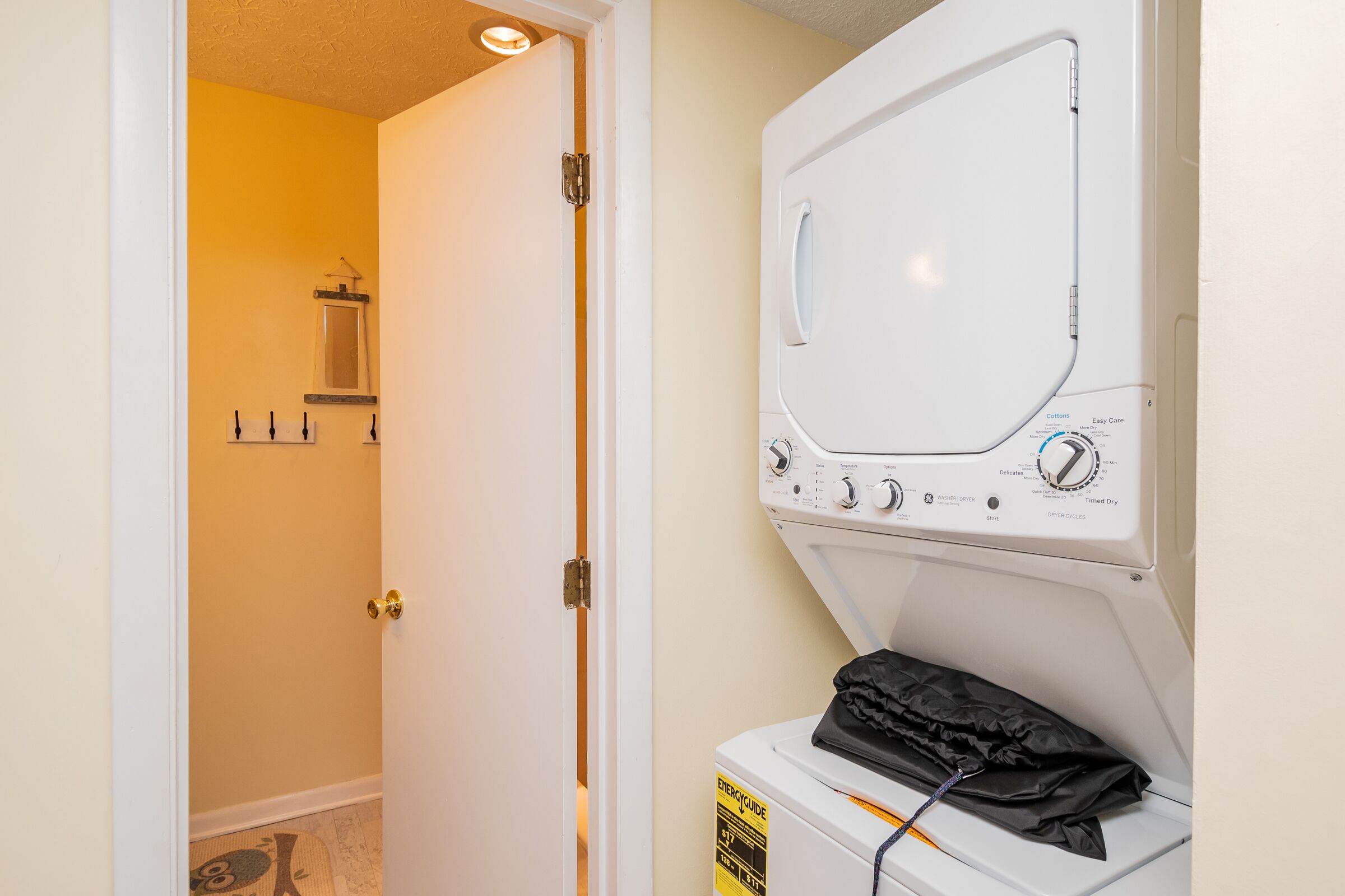A laundry room with a front-loading washer and dryer, a door leading to a bathroom, and a small window above the sink.