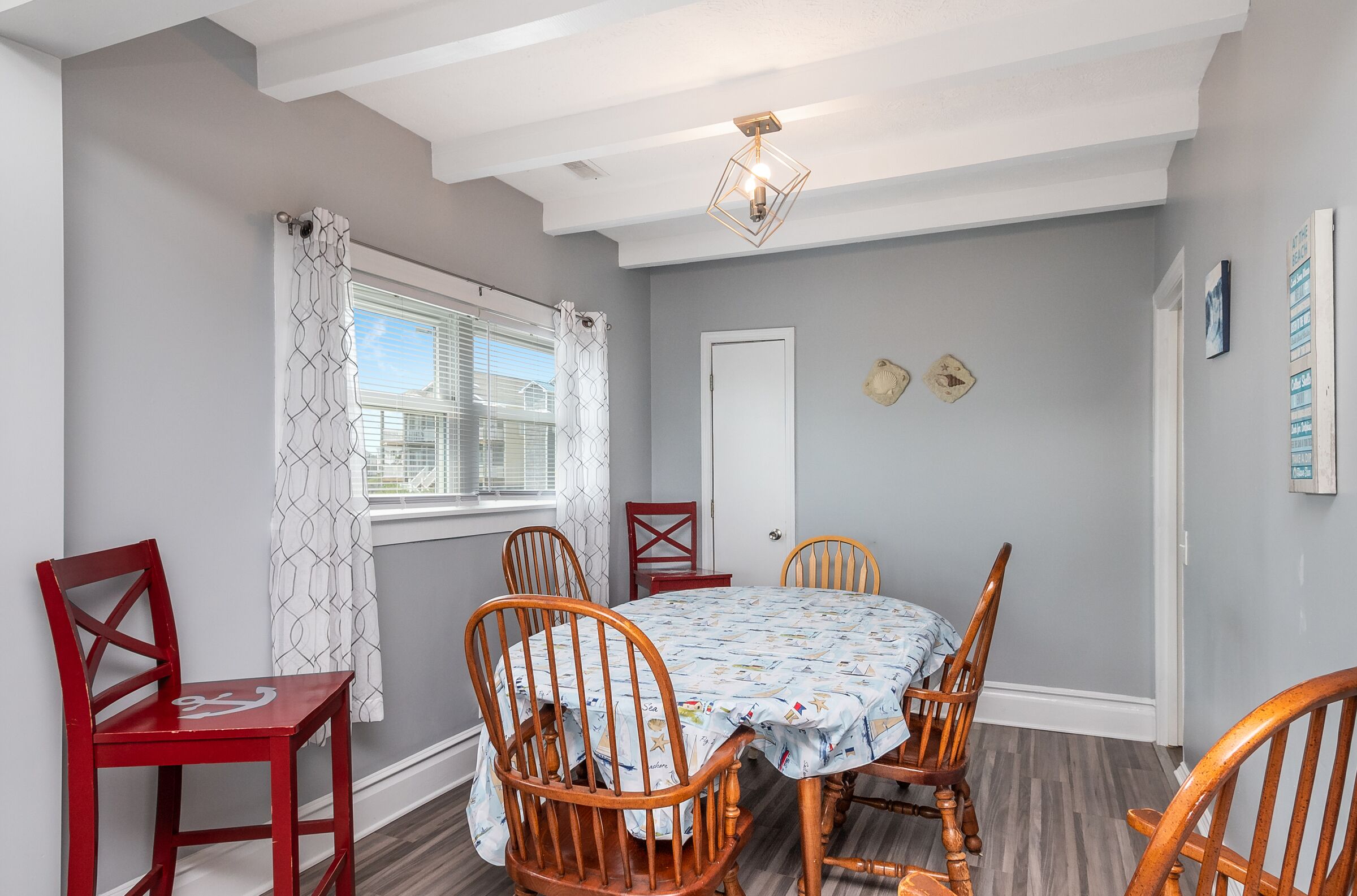 A dining area with a round table, wooden chairs, a patterned tablecloth, and a geometric ceiling light fixture.