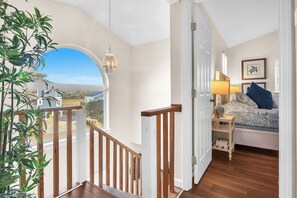 A bedroom with a bed, bedside table, lamp, and a view through an open door. - Atlantic Delight: Dog-friendly Home in Quiet Area Within a Few Blocks of Beach (Oak Island)