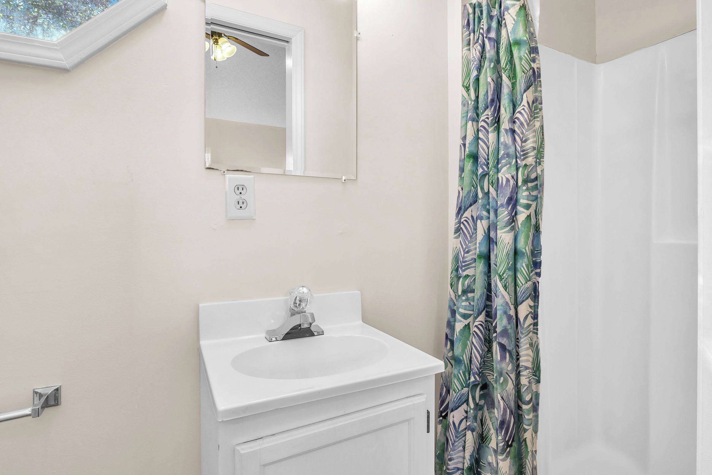 A bathroom with a white sink, a mirror, and a shower curtain with a leaf pattern.