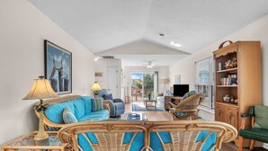 Ein geräumiges Wohnzimmer mit einem blauen Sofa, Korbstühlen, einem Holzregal und einem Fernseher.