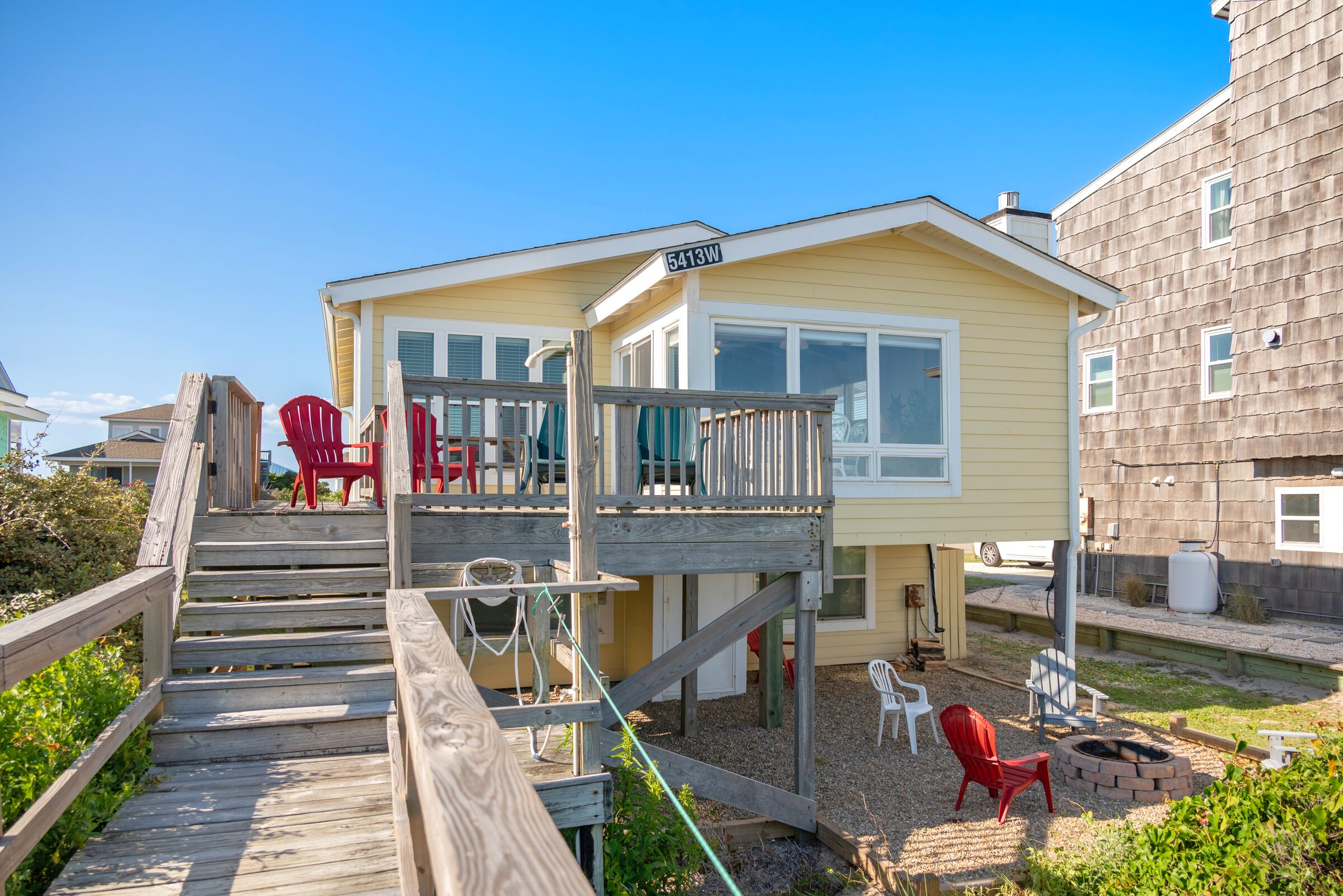 Ein Strandhaus mit Holzterrasse, Sitzgelegenheiten im Freien und einer Feuerstelle.