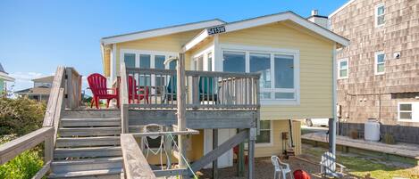 Ein Strandhaus mit Holzterrasse, Sitzgelegenheiten im Freien und einer Feuerstelle.