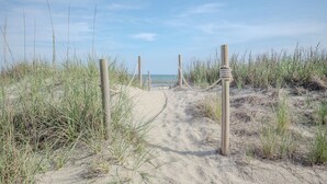 Un sendero arenoso que conduce al mar, bordeado por hierba y postes de madera.