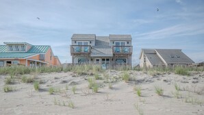 Propiedad frente a la playa con una casa de dos pisos, balcones, arena en primer plano y cielo despejado.