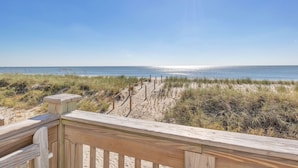 A wooden deck overlooking a beach with sand dunes and the ocean.