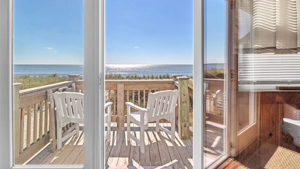 A wooden deck with two white chairs overlooking a beach.