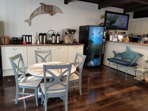 Una cocina con armarios blancos, una mesa de comedor con sillas, una cafetera y un refrigerador con puerta azul.