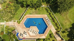 Vista aérea de una piscina rodeada por un jardín con sillones de descanso y una pequeña terraza.