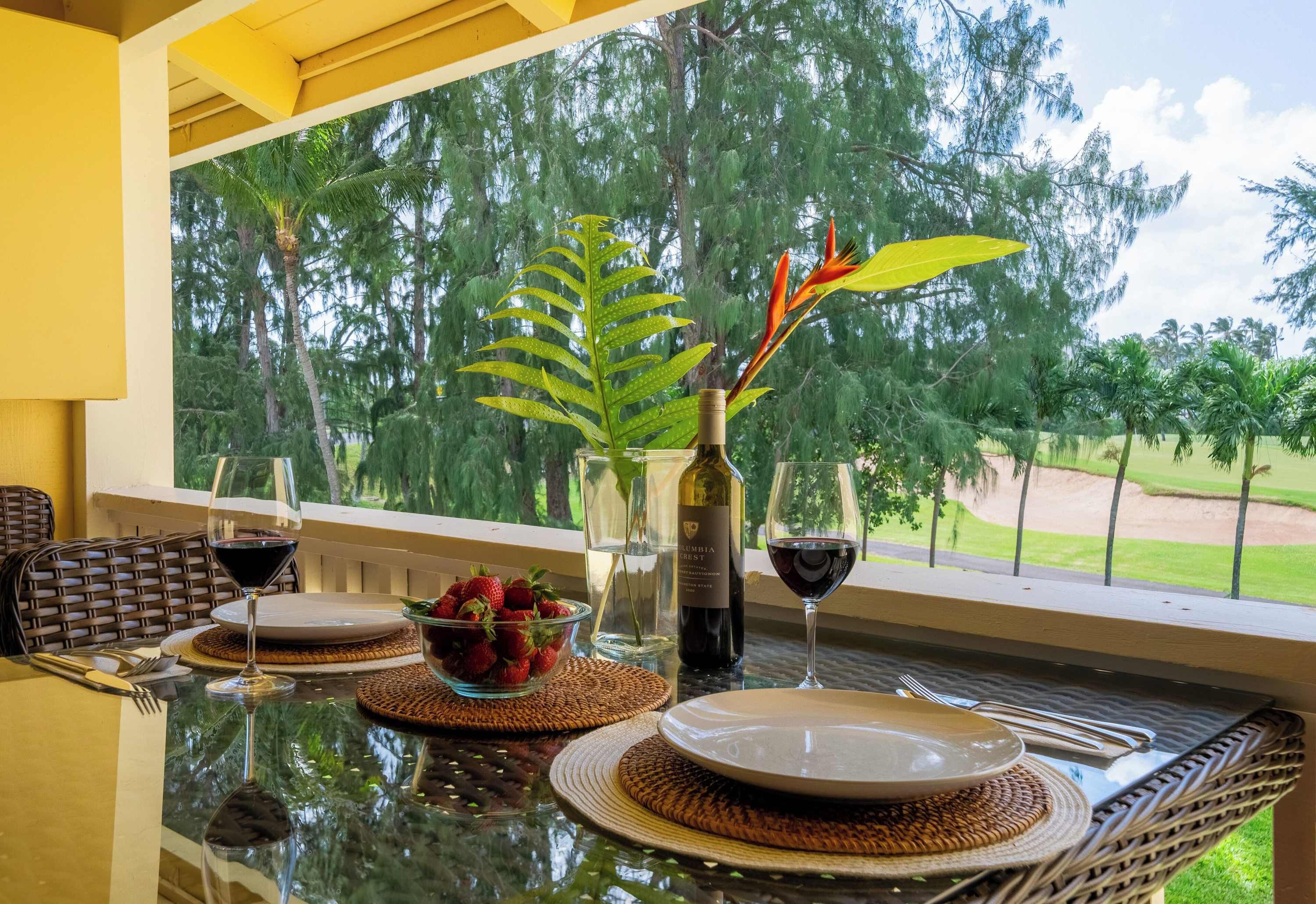 Mesa de comedor servida con platos, vasos y una botella de vino, con vista a árboles y un campo de golf a través de una ventana.
