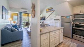 Una cocina moderna con armarios blancos, un refrigerador de acero inoxidable y un horno. Hay un rincón comedor con un sofá azul y una escalera que lleva a otro nivel.