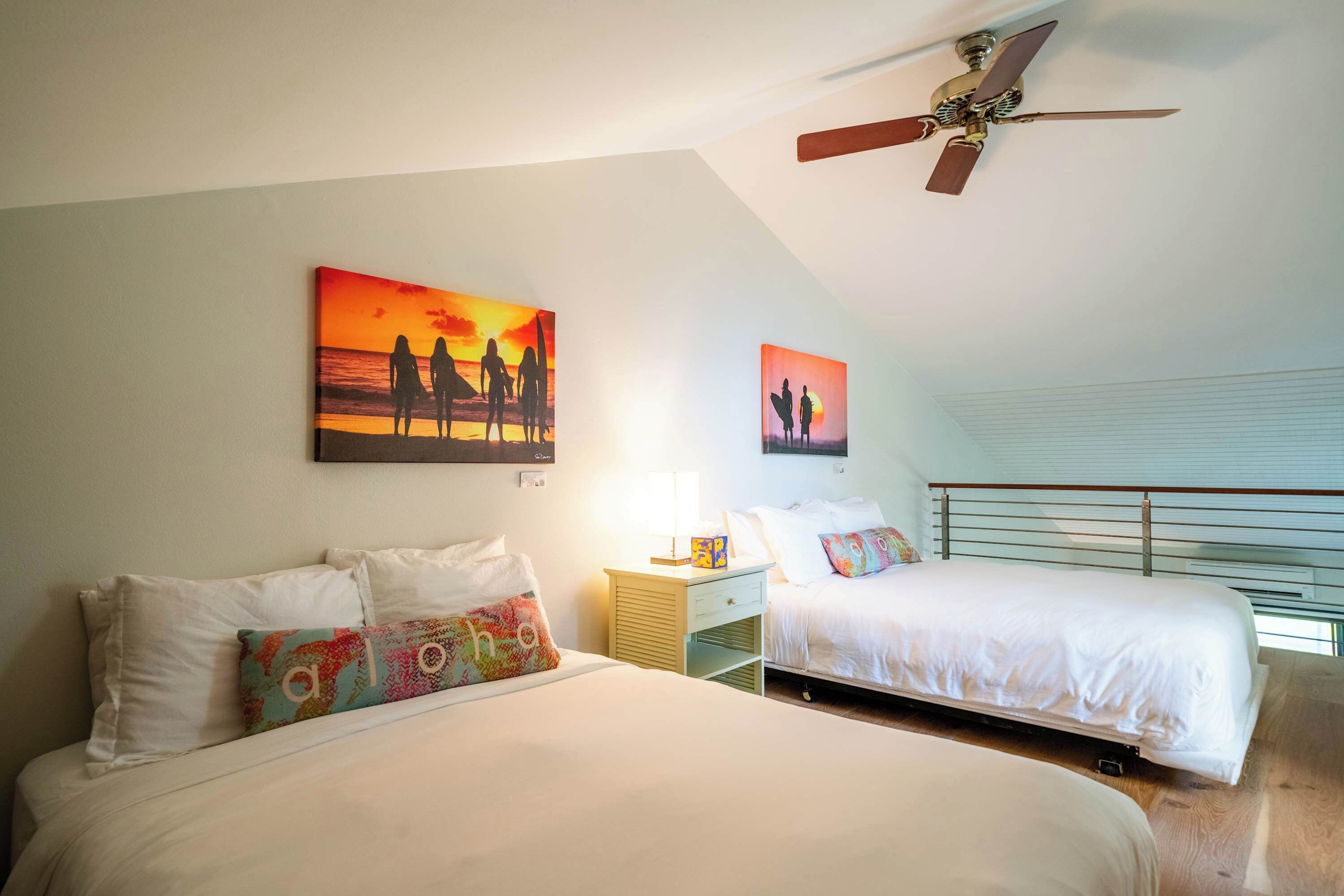 Habitación de hotel con dos camas, ventilador de techo y una obra de arte que representa un atardecer.