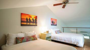 Habitación de hotel con dos camas, ventilador de techo y una obra de arte que representa un atardecer.