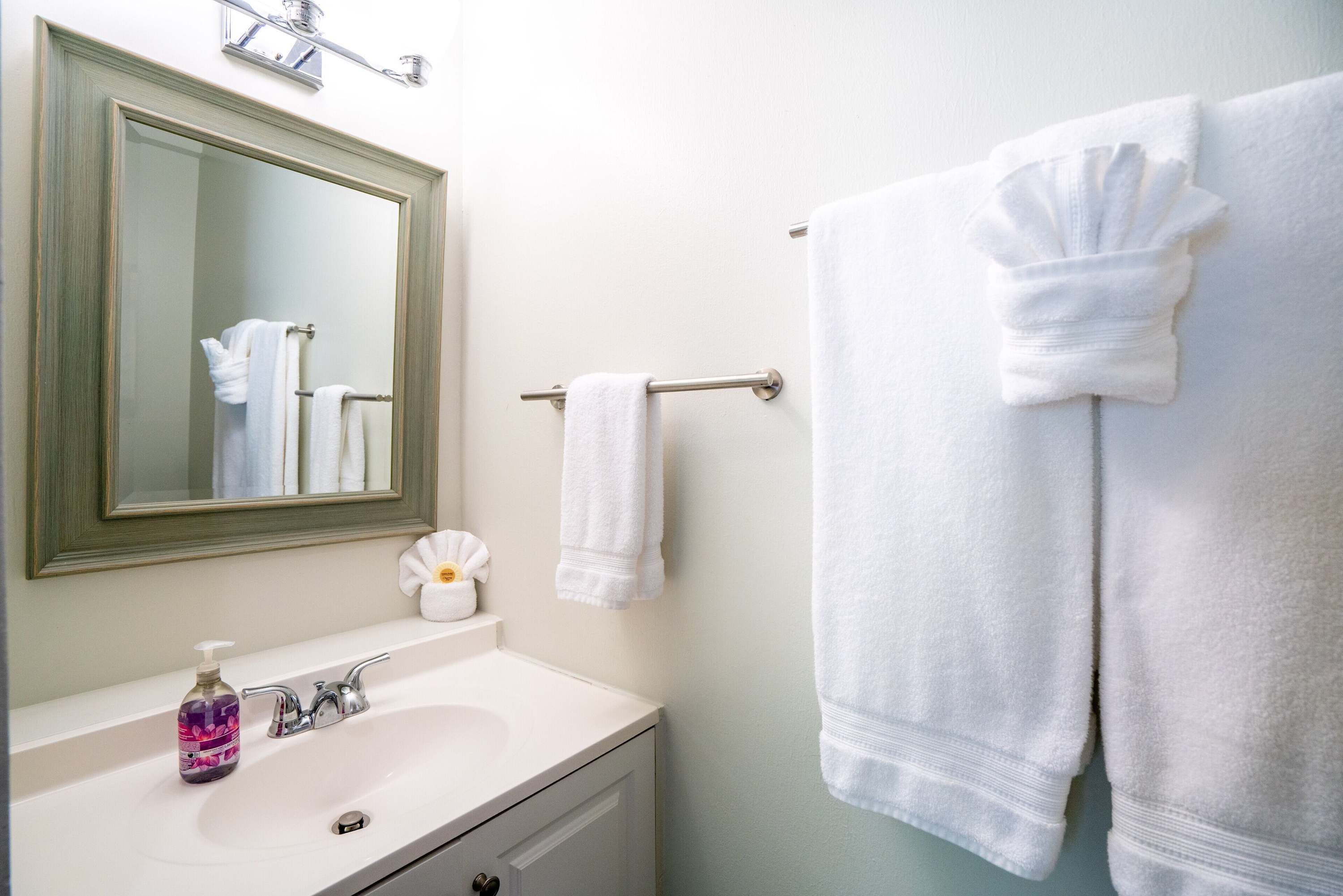 Une salle de bain avec un lavabo blanc, un miroir et deux serviettes blanches suspendues à une barre à serviettes.