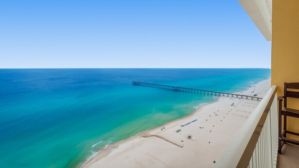 A beach with a pier extending into the ocean, a sandy beach, and a clear blue sky.