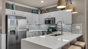 A modern kitchen with white cabinets, stainless steel appliances, a large island with bar stools, and decorative items on the wall.