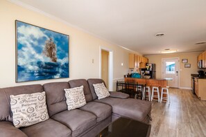 A living room with a brown sectional sofa, a coffee table, and a large painting of a sailboat.