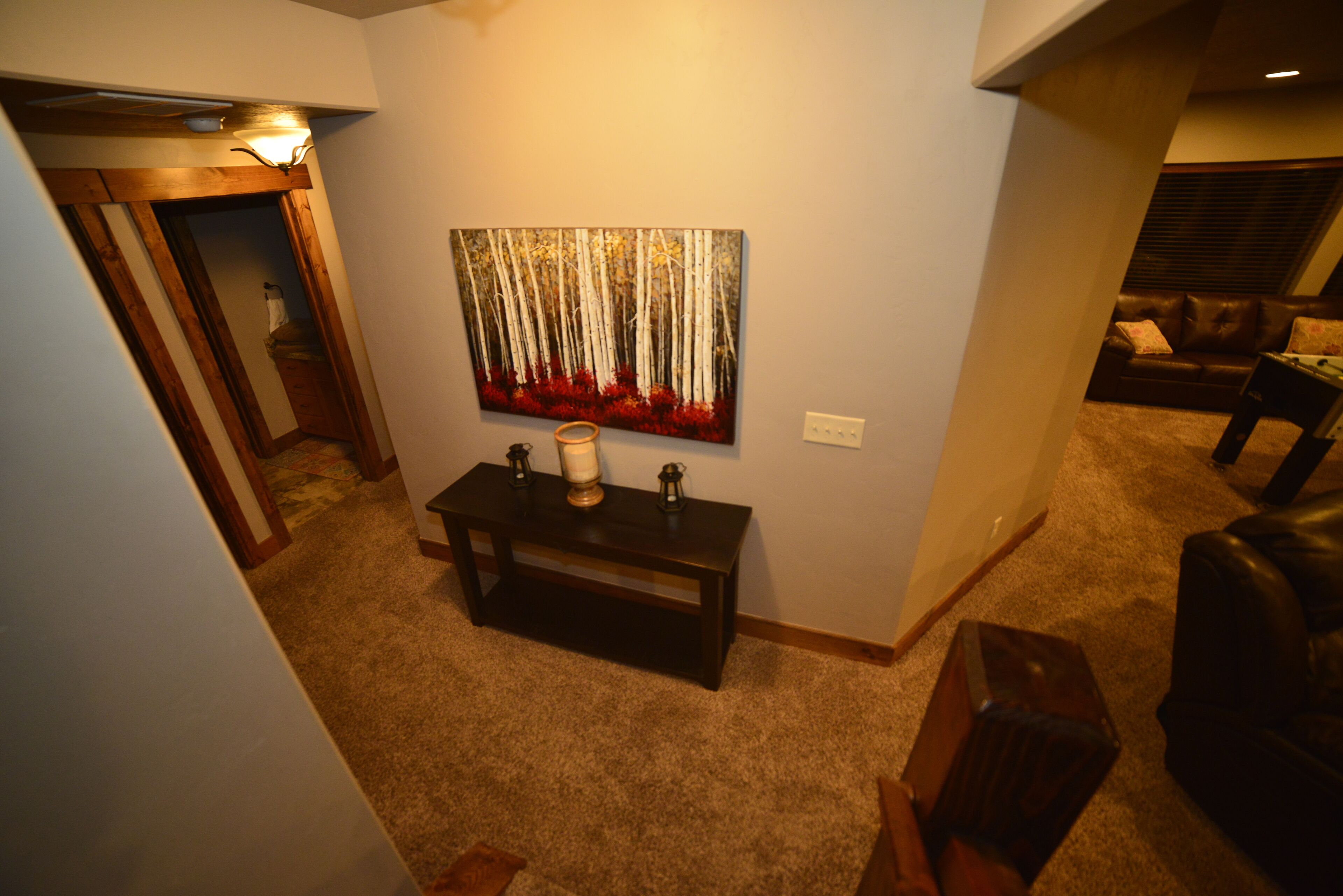 A hallway with a wooden bench, a painting of trees, and a couch in the background.