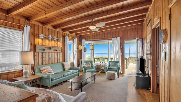 Une cabane en bois spacieuse avec un plafond haut, un salon confortable doté d’un canapé vert, d’une table basse et d’un téléviseur.