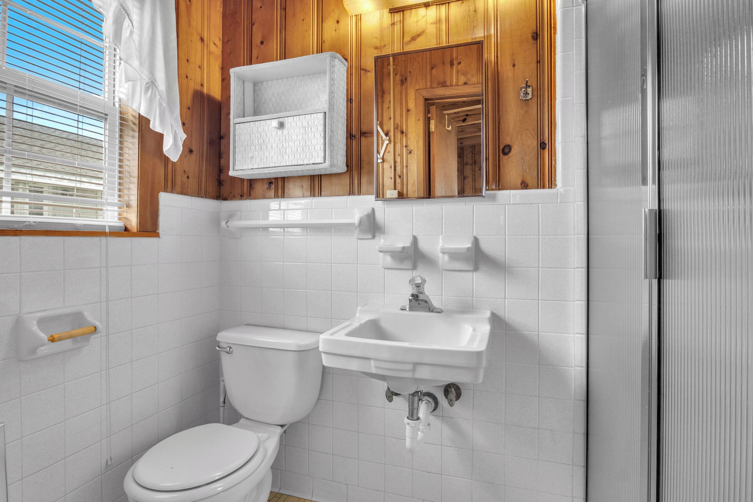 A bathroom with a toilet, sink, and wooden paneling.