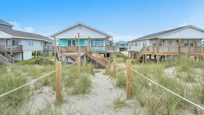 Une propriété située en bord de mer, avec des passerelles en bois menant à des maisons de plage, chacune dotée d’un balcon et d’un drapeau.